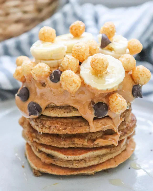 Fluffy pancakes topped with banana, peanut butter, chocolate chips, and Schoolyard Snacks cereal.