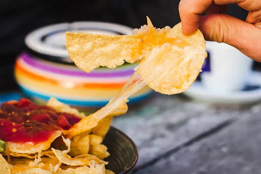 Schoolyard Snacks baked cheddar protein puffs spilling out of a colorful snack pack on a wooden surface.